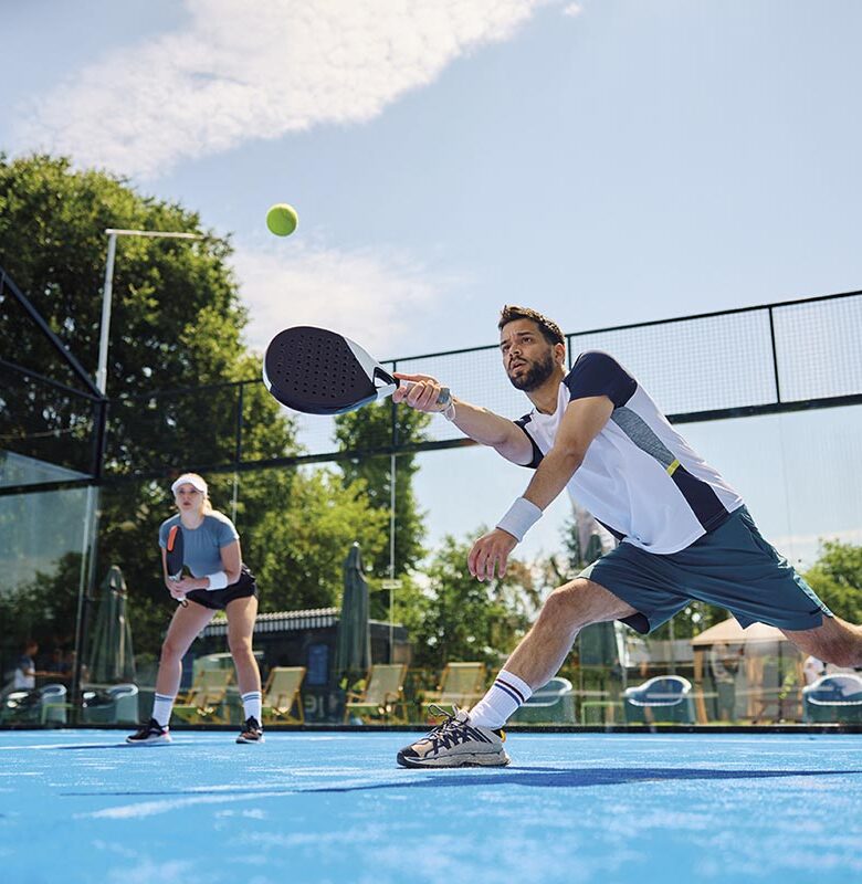 Paddle tennis player making an effort to while hitting ball during match on outdoor court.