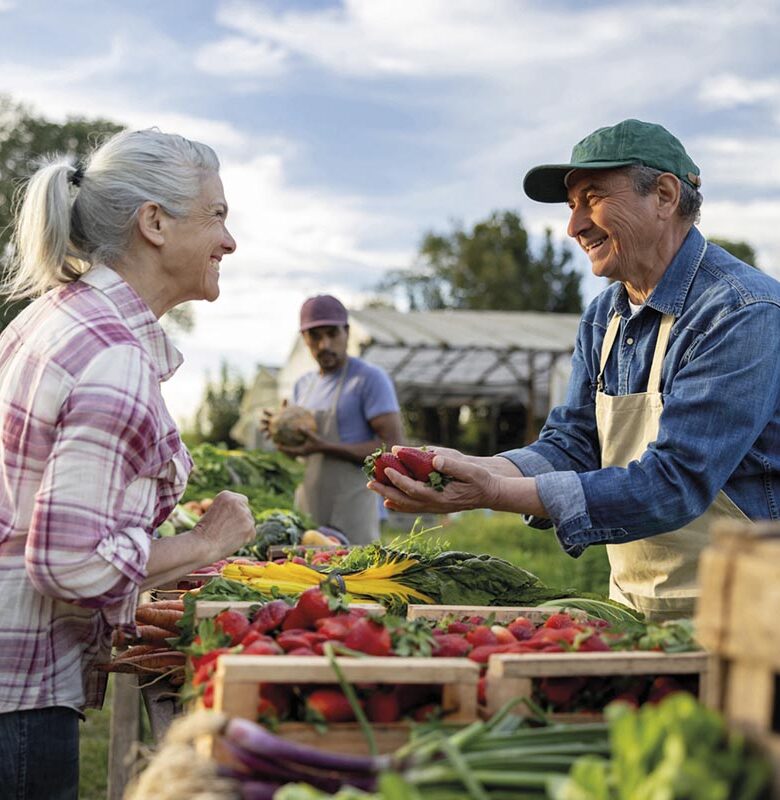 Happy farmer selling organic strawberries to a client at a Farmer's Market